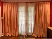 Full view of all four curtain panels (two pink pleated outer and two sheer ivory inner) on brass double rod across window.