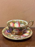 Front view of Aynsley tea cup and saucer set showing detailed fruit pattern and gold trim