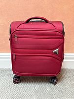 Front view of the compact red carry on suitcase showing zippered pockets and logo plate