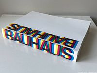 Side view showing the thickness of the white softcover book with colorful BAUHAUS text on the spine.