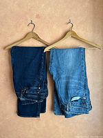 Two pairs of blue Levi's jeans folded and hanging on wooden hangers showing different denim shades.