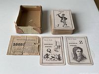 Photo showing 56 cards stacked, three individual cards including 'Q' and 'Z' prize cards featuring Victorian character illustrations, partial instruction sheet with text titled 'Logomachy War of Words', and a worn brown cardboard box.