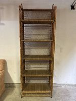 Front view of five-tier tall rattan shelf showing woven lattice sides and back, flat rattan shelves, standing against wall.