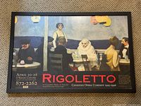 Full view of the framed poster showing the Rigoletto opera advertisement with text and image of people in a seated scene.