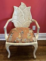 Photo of vintage painted carved wood chair showing front view with leaf motif backrest and patterned upholstered seat. Left arm with visible wear and needing repair.