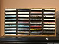 Front view showing the oak laminate wood CD rack with approximately 60 vintage music CDs arranged upright across 4 columns