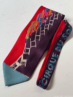 Full view of the folded silk tie with colorful ladder and figure design, showing red, purple, and blue colors with a teal tip.