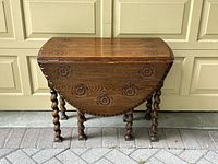 Front view of vintage drop leaf table showing barley twist legs and floral carvings on the closed drop leaves.