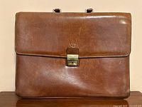 Front view of the vintage brown leather briefcase with locking clasp and embossed logo above clasp