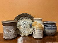 Four vintage studio pottery pieces arranged side by side on wooden surface against orange wall