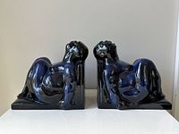 Pair of glossy blue pottery bookends shaped as reclining men, viewed from front on a white surface.