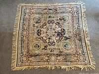 Full view of square textile, showing overall design with fringe edges and visible damage including tears and holes.