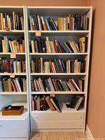 Full view of the white modular bookcase right section loaded with books and showing the overall structure, shelves, and drawer location
