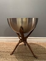 Front view of the metal bowl on the wooden tripod stand showing the silver exterior of the bowl and the carved wooden legs of the stand.