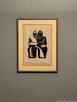 Front view of the framed linocut print showing the tiki figure in black and white with mat framing and black frame on a gray wall.