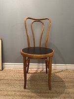 Front view of mid century bentwood oak chair with black round seat showing curved backrest and slender legs.