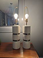 Full view of two lit ceramic table lamps on wooden surface in front of a mirror, showing shape and light output.