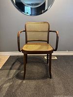 Front view showing curved armrests, woven cane seat and backrest.