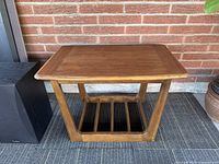 Front and side angle view of mid century modern walnut side table on rug with brick wall background.