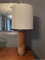 Modern table lamp with faux fur cylinder base and white drum shade shown unlit on wooden surface.