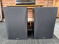 Pair of Infinity SM-85 speakers with grille covers on, showing black fabric fronts and black wood grain finish on cabinet sides.