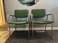 Front view of two tubular steel chairs with green upholstery, showing postmodern design and chrome frames.