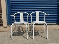 Front view of two white IKEA Maxmö metal chairs showing perforated circular seats and curved armrests.