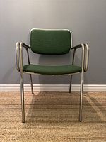 Front view showing vibrant green upholstered seat and backrest framed by tubular steel and integrated armrests.