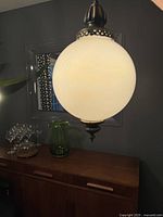 Front view of hanging vintage glass globe light fixture above wooden sideboard, showing the pearlescent white globe and metal details.
