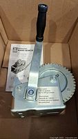 Hand winch with handle and gear visible in box