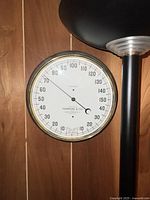 Round antique marine barometer with white face, black numbering from 28 to 31 inches mercury, needle indicator, brass bezel, mounted on wood panel.