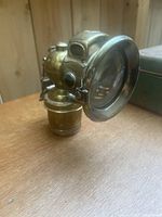 Side angle view of the brass lamp with large glass front and curved body placed on wooden surface.