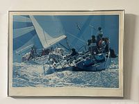 Framed art print showing a detailed image of a sailboat regatta on water with bright sparkling highlights. The frame is metallic with a white matte border. The photo shows the front view of the artwork.
