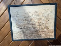 Close-up of the hand carved wooden sailing ship artwork framed in black.