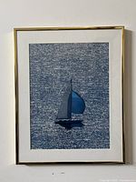 Front-facing photo showing the framed abstract art of a sailboat on water with predominant blue tones, mounted on a white wall.