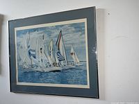 Photo taken showing one framed print depicting multiple sailboats on blue water under partly cloudy sky, matted blue and framed behind glass, signed R.M. Carter.