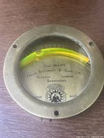 Top-down photo of the circular brass inclinometer showing the liquid-filled curved level and measurement scale under glass, with visible maker's marks and trademark.