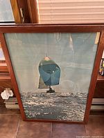 Framed vintage sailboat art print leaning against window with sunlight reflections.
