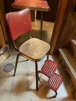 Vintage metal folding kitchen chair with wooden seat and backrest, chrome frame, and attached footrests shown from an angle.
