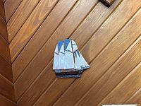 Photo of a handcrafted wooden sailboat wall art mounted on a slanted wood-paneled wall, showing the piece's colors and condition.