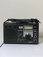 Front view showing full radio, speaker grille, control panel, carry strap