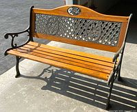 Front perspective of wood and cast iron bench showing seat slats, iron arms, decorative back panel
