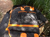 Black quilted seat cover with orange trim folded to show quilted surface and zipper