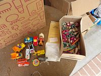 Group view of plastic vehicles, figures, spinning top, boats, goose figure, cloth bag, manila envelope and box of wooden pieces