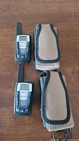 Two Cobra MicroTALK walkie-talkies and two beige carrying cases on wooden surface.