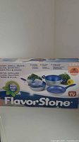 Box front showing Flavor Stone cookware set with blue interior and silver exterior, includes three pans and a lid.