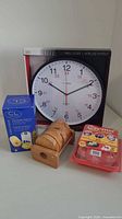 Photo showing all four items together: wall clock in box, blue box for egg cooker, wooden coasters stacked, red kitchen tool set packaged
