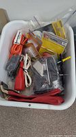 White plastic bin containing various tools and hardware items including gloves, extension cords, electrical cords, packaged hardware components, and loose fittings.