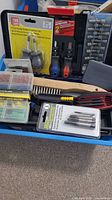 Overview of the blue toolbox with assorted hand tools inside, including screwdriver bit sets, ratcheting screwdrivers, and small hand tools in packaging.