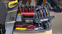 Top view showing various hand tools including pliers, screwdrivers, and a saw in a black plastic tray with red handle